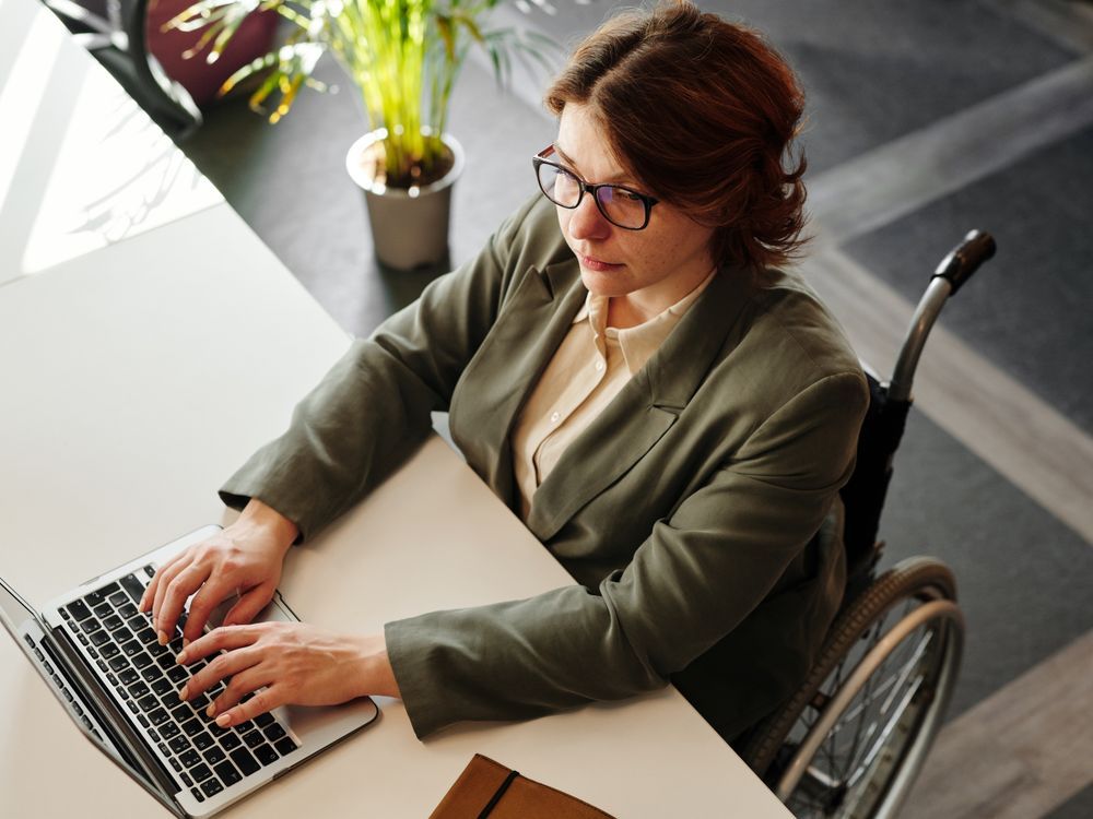 Mulher em cadeira de rodas digitando no notebook no escritório